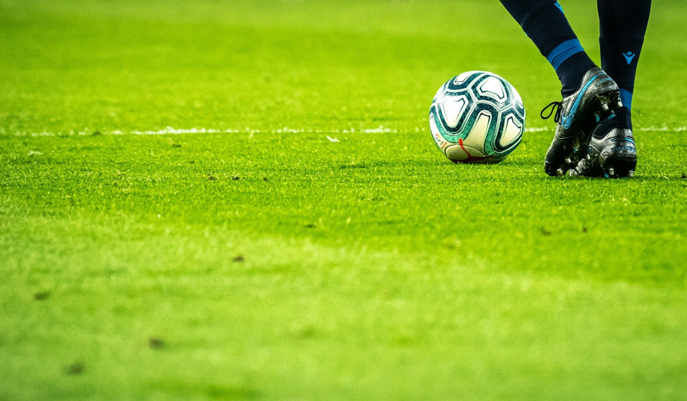 feet of male soccer player on the field beside a soccer ball